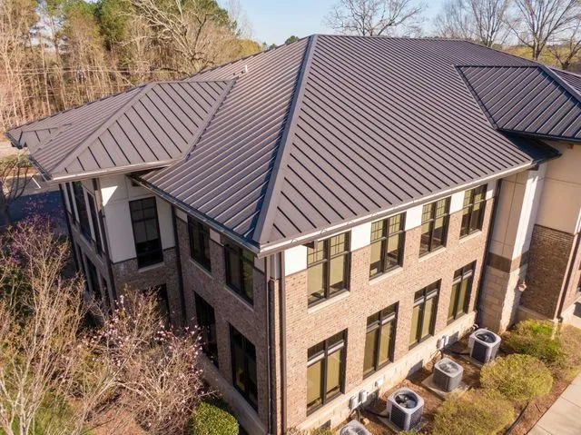 An aerial view of a brick commercial building with a dark metal roof, large windows, and outdoor HVAC units.