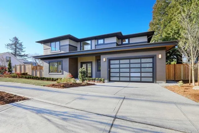 Modern two-story suburban home with a multi-paneled glass garage door and a concrete driveway under a clear blue sky.