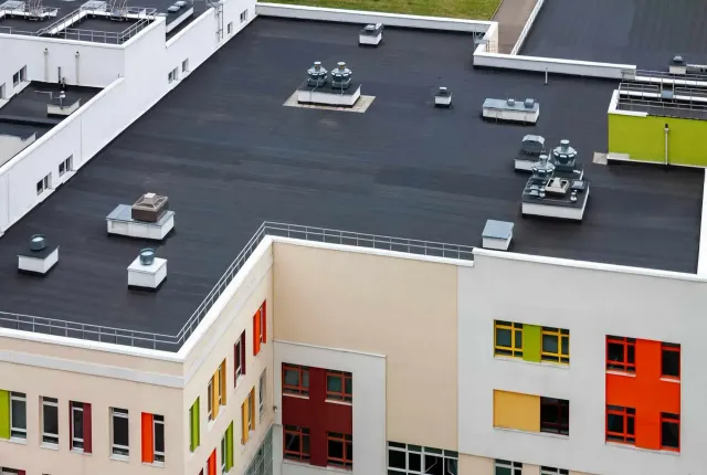 Aerial view of a modern school building with a black roof, white walls, and colorful window panels.