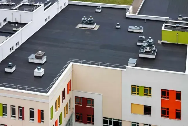 A high-angle view of a flat, black roof on a modern building with colorful window accents.