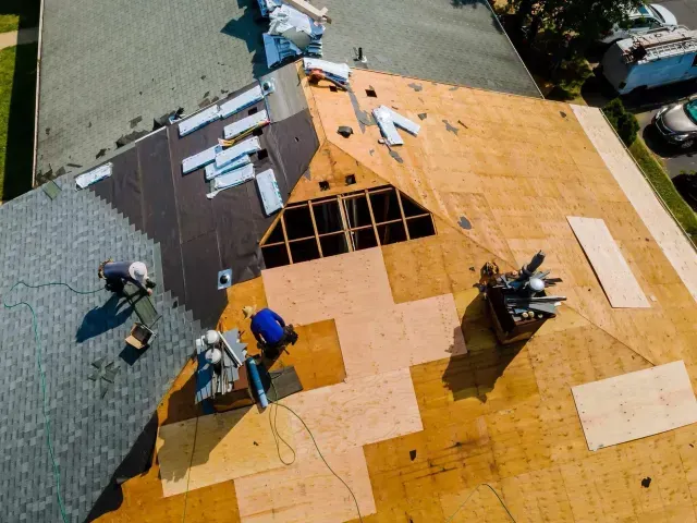 Roof repair contractors in Aurora, IL replacing shingles on a house roof with exposed wooden sheathing and a chimney.