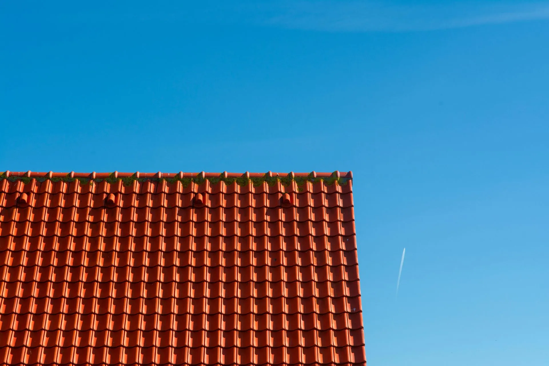 Two construction workers wearing safety vests and hard hats install solar panels on a tiled residential roof.